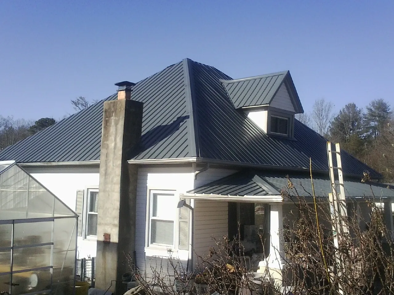 Dark blue standing seam metal roof on a white farmhouse with dormer — Slate & Tile Roof Repair by Roofing Brothers in Charlotte