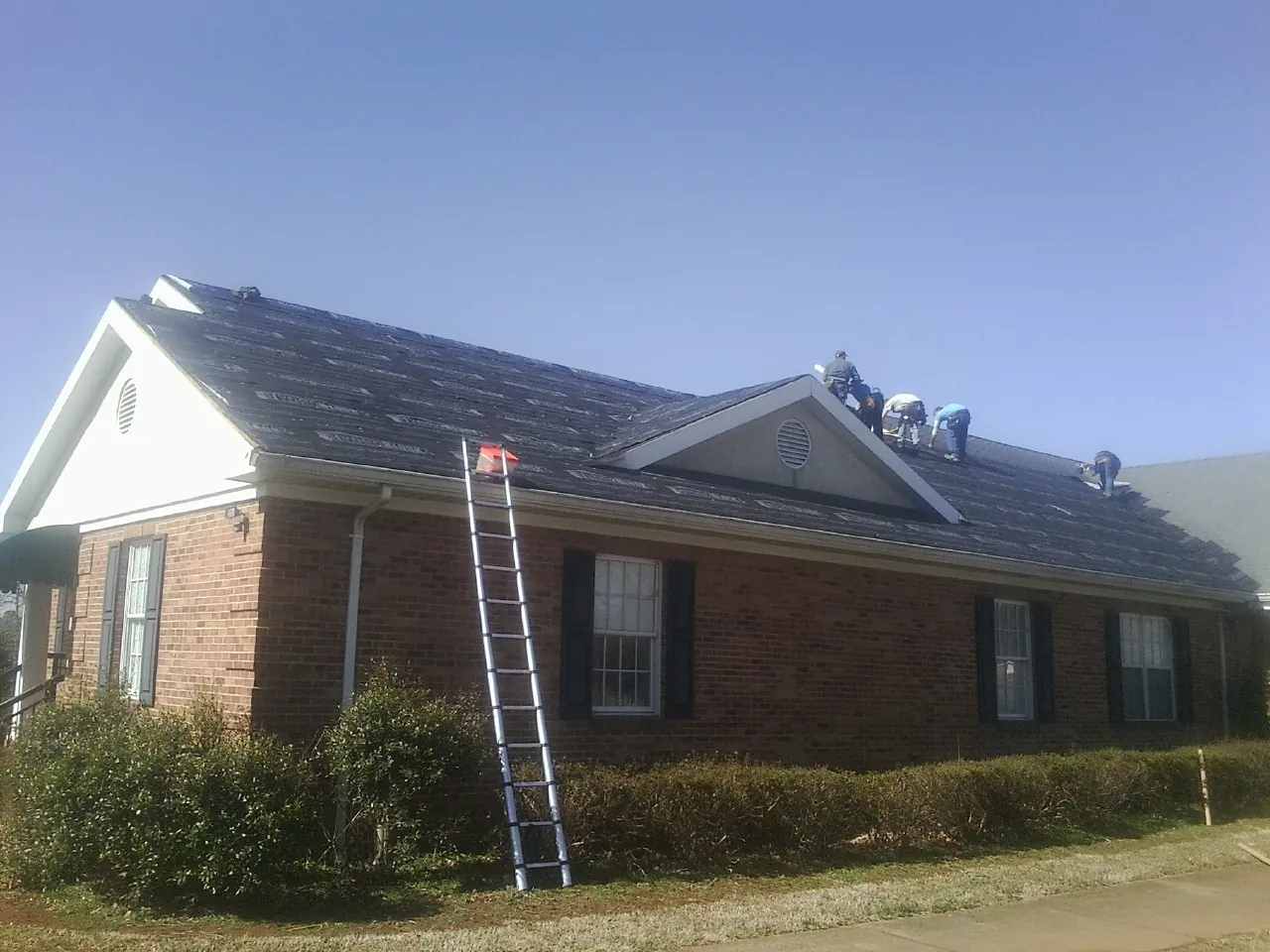 Crew tearing shingles off a brick ranch roof with a ladder set — Emergency Roof Repair work by our crew in Charlotte