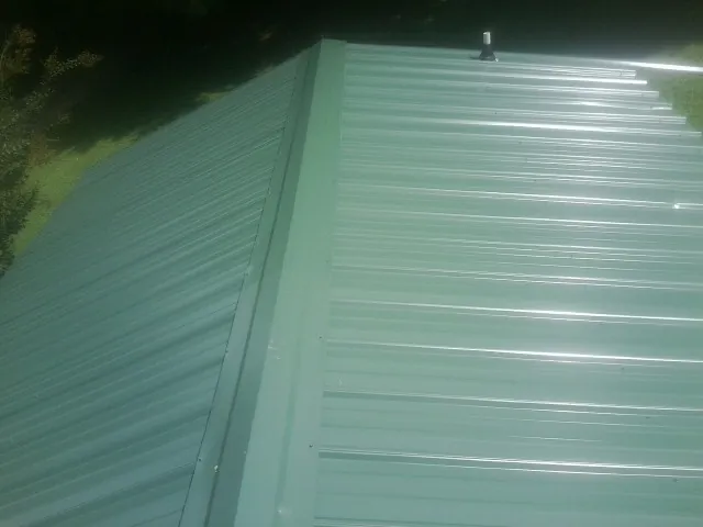 New green metal panels meeting at the ridge of a roof — Flat Roof Repair work by our crew in Charlotte