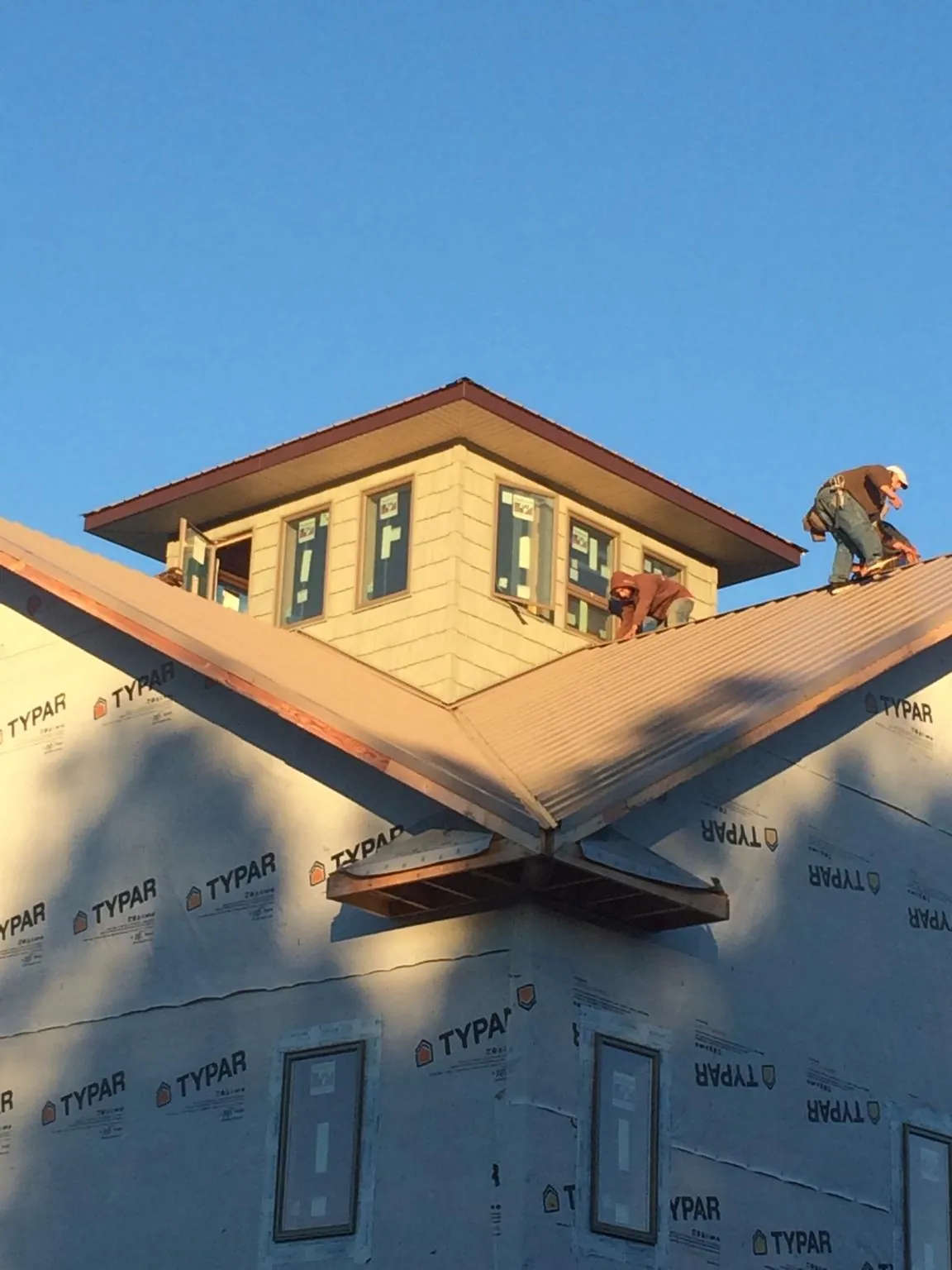 Roofers working around a rooftop cupola on a new metal roof at sunset — Roof Waterproofing in Charlotte by Roofing Brothers